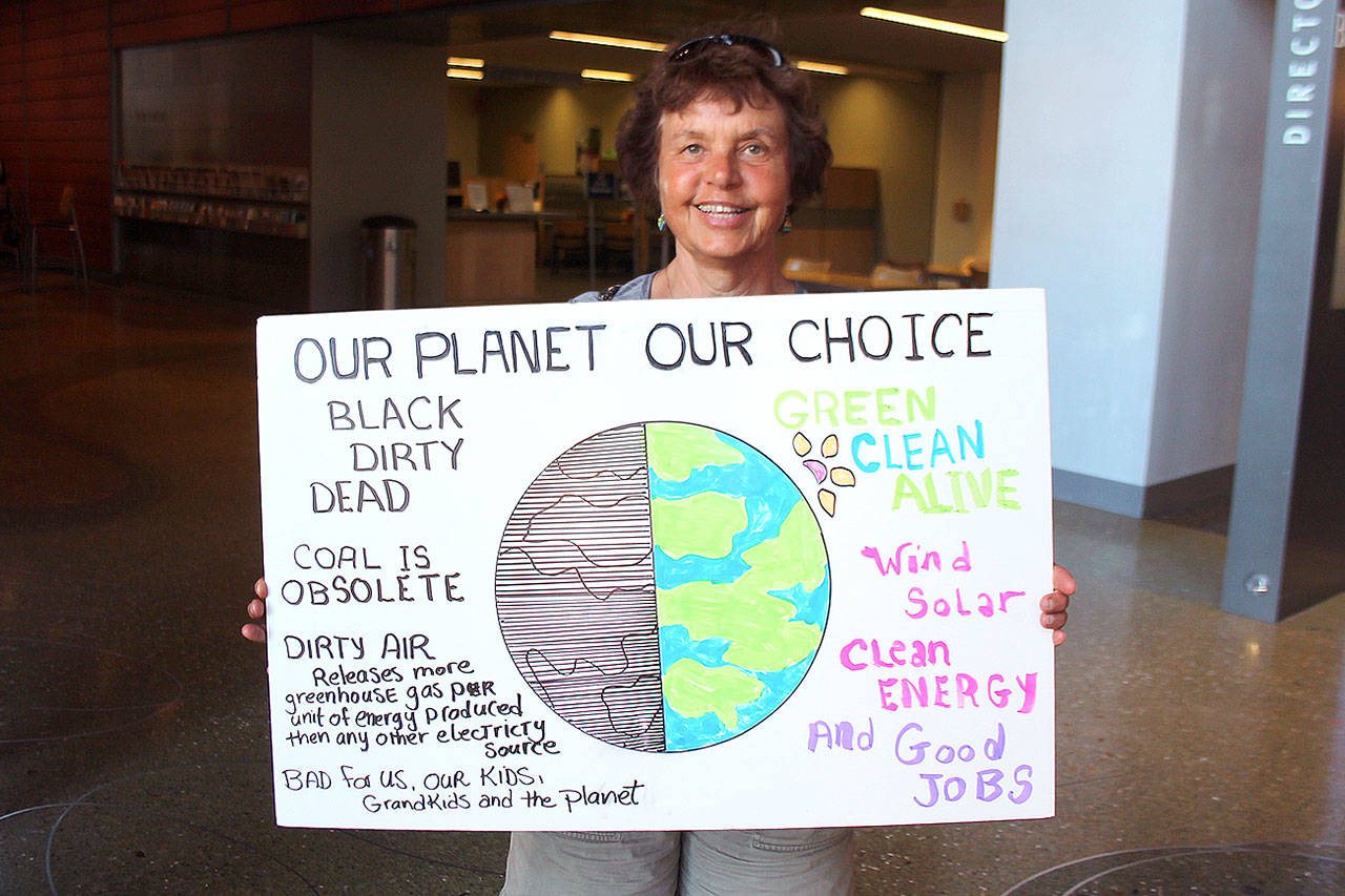 Linda Baker of Renton stands outside of the Bellevue City Hall council chambers holding a sign promoting clean energy. Photo by Raechel Dawson