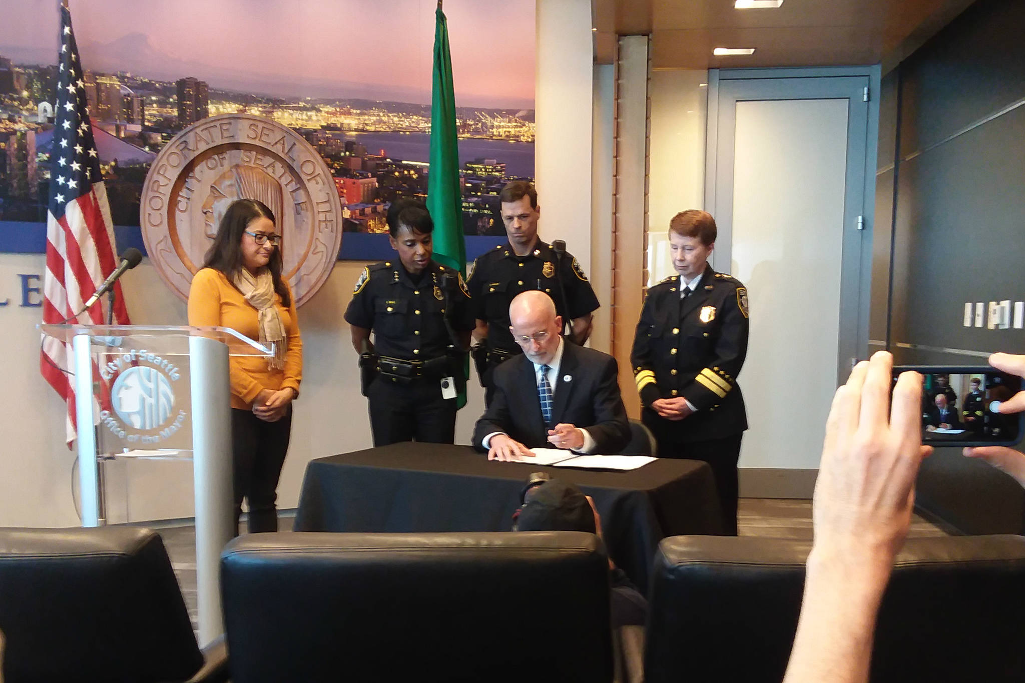 Mayor Tim Burgess signs the executive order to limit and begin further reform of moonlighting by Seattle police, flanked by Councilmember M. Lorena González and SPD command staff.